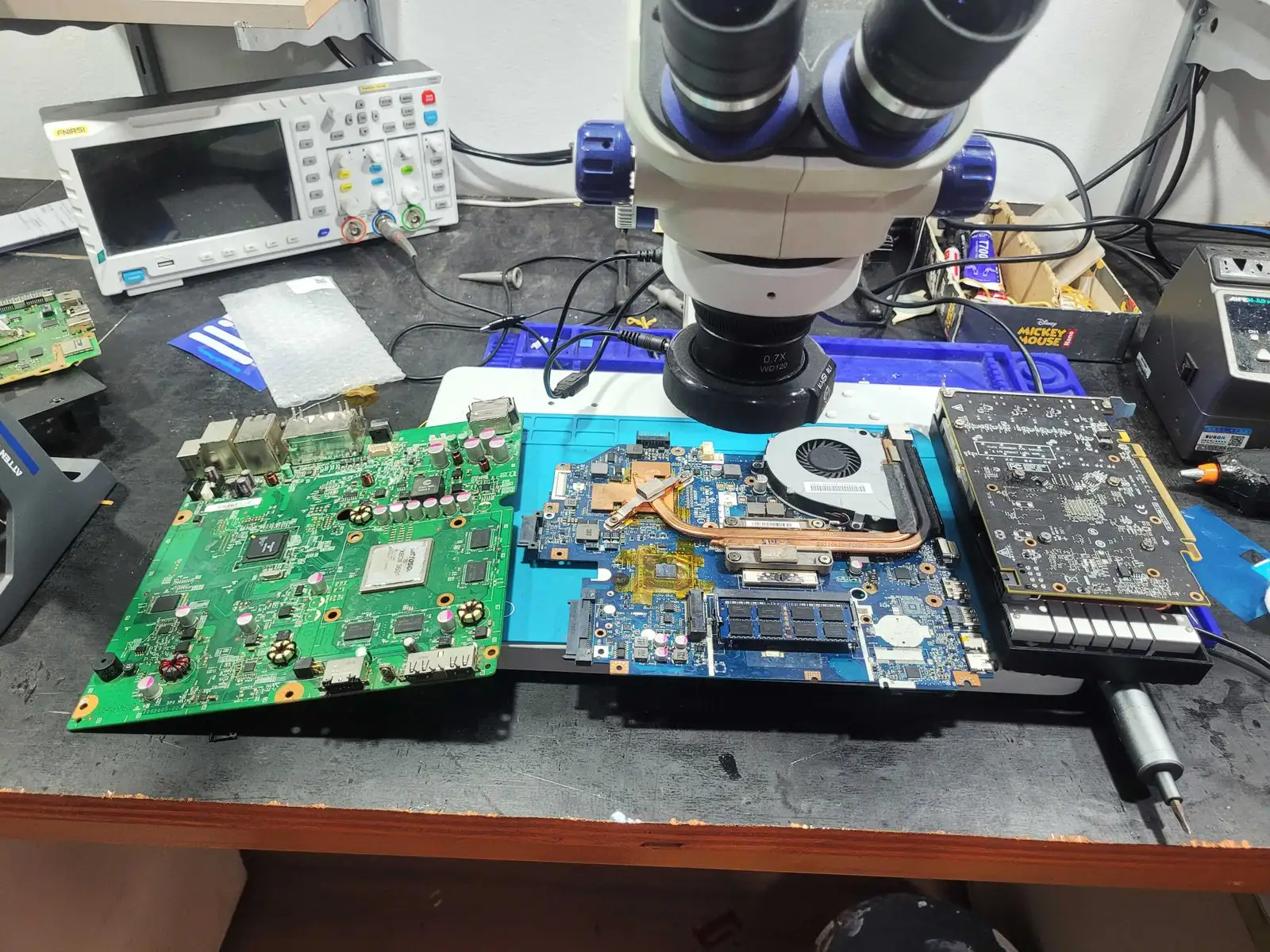 Placa de console, placa-mãe de notebook e placa de vídeo sob o microscópio, com osciloscópio ao fundo